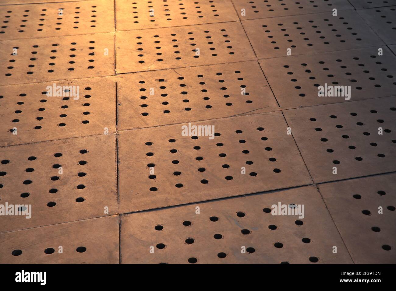 Carreaux de pavage en béton avec trous réguliers sous lumière tungstène. Image d'arrière-plan. Banque D'Images