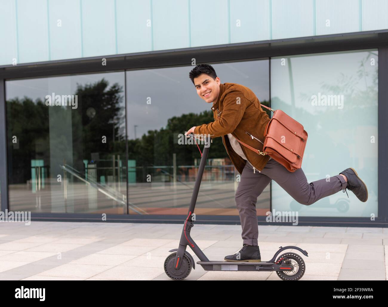 jeune garçon avec un porte-documents marron conduisant le scooter électrique avec une jambe Banque D'Images