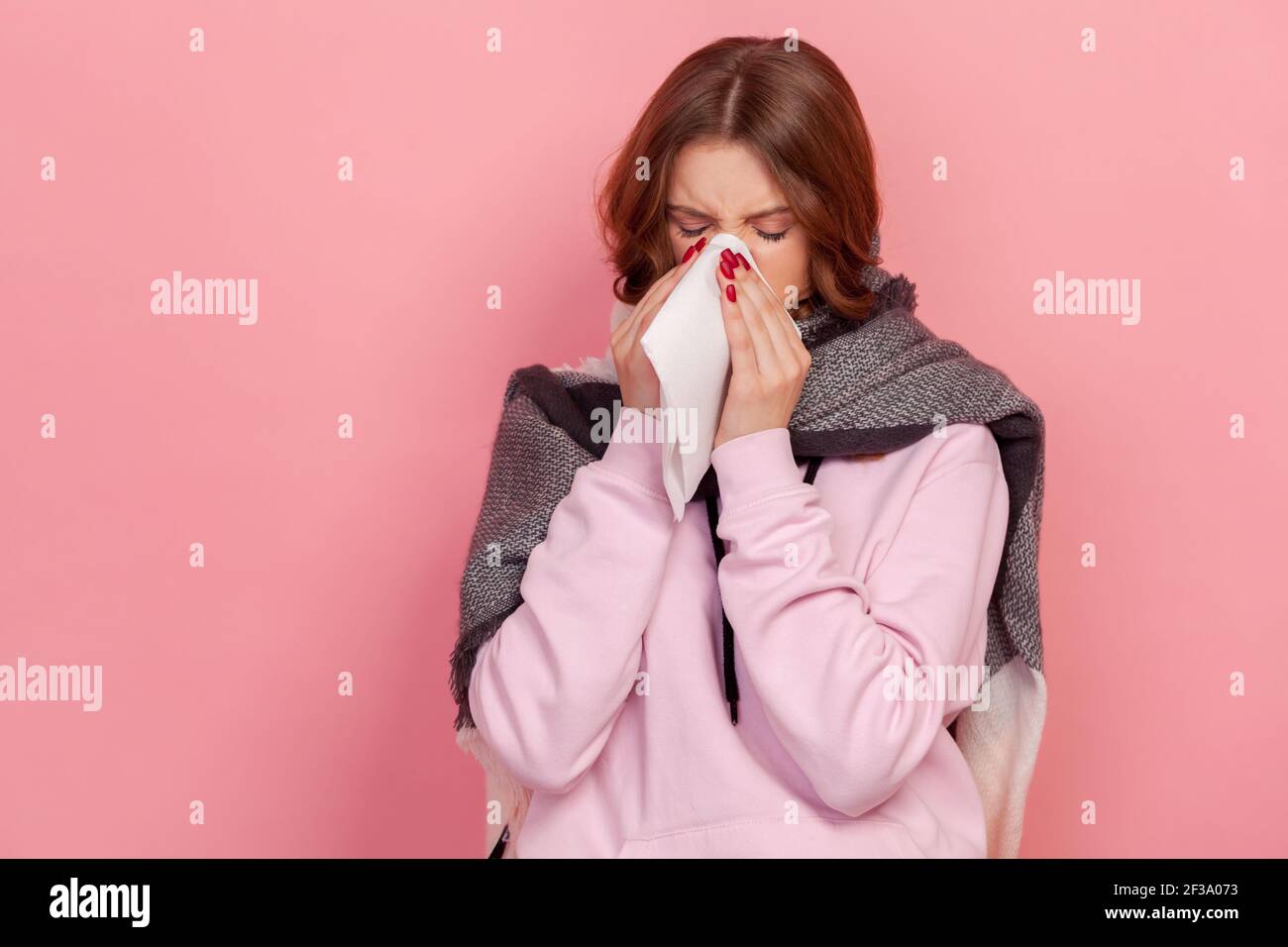 Portrait d'une adolescente malade à cheveux bouclés enveloppée d'un foulard éternuant dans une serviette, nettoyant le nez et la toux, souffrant de grippe. IND Banque D'Images