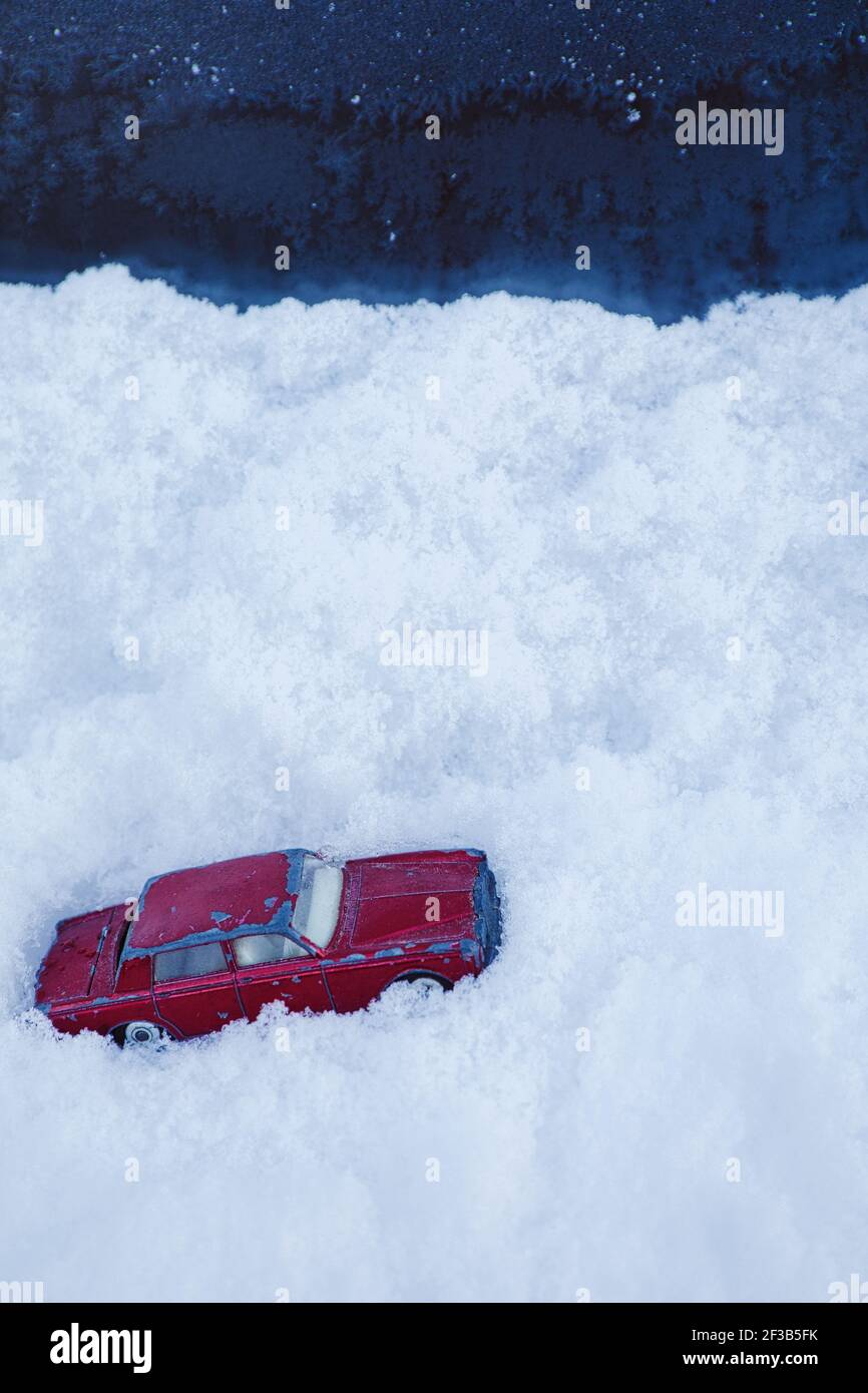 Voiture jouet rouge coincée dans un blizzard de neige profonde. Concept de piégé, changement climatique, temps extrême Banque D'Images