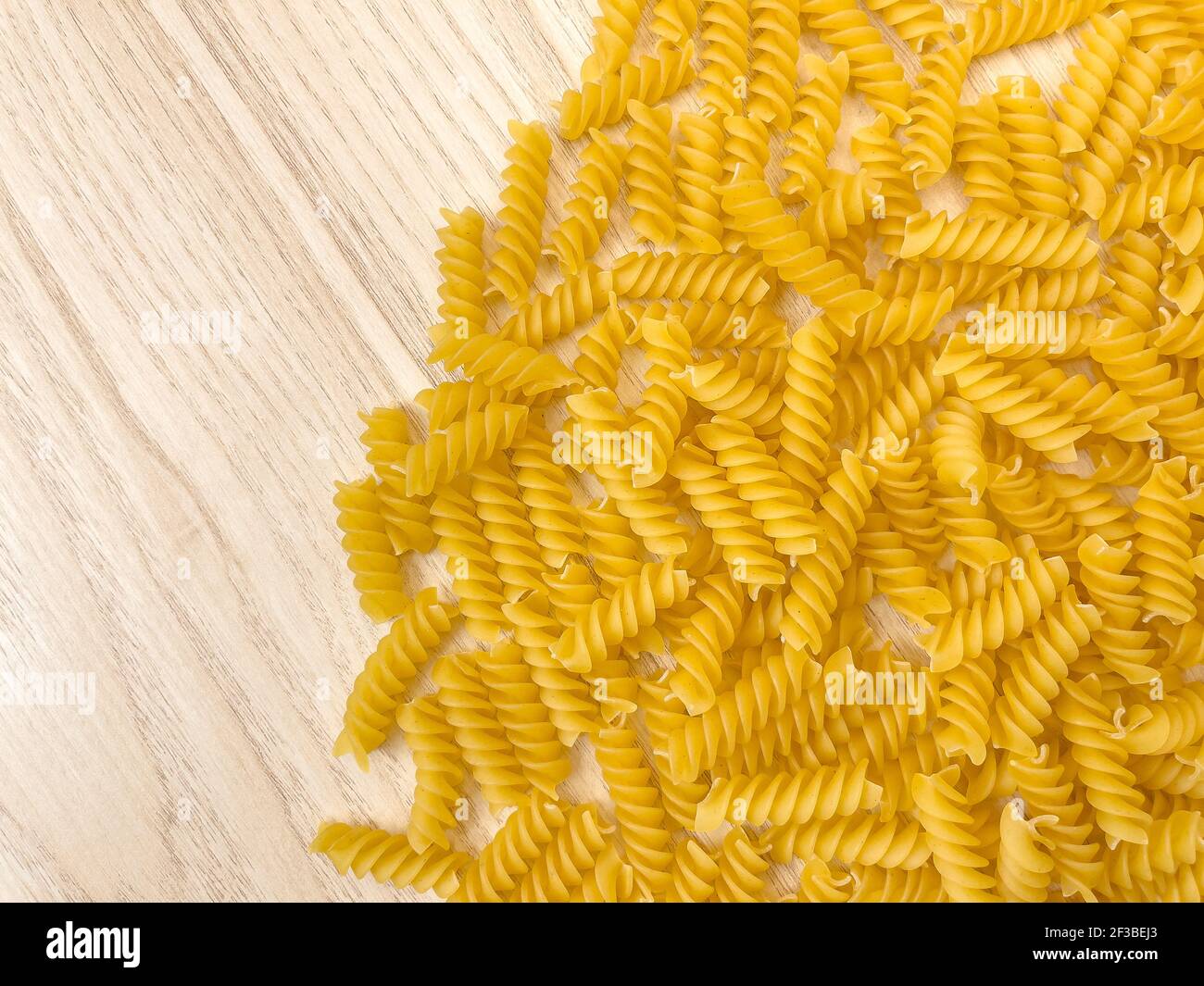 Fond ou texture de la nourriture pâtes italiennes sèches crues en forme de spirale sur une table ou un bureau en bois. Gros plan, macro, vue de dessus. Macaroni non cuit. Banque D'Images