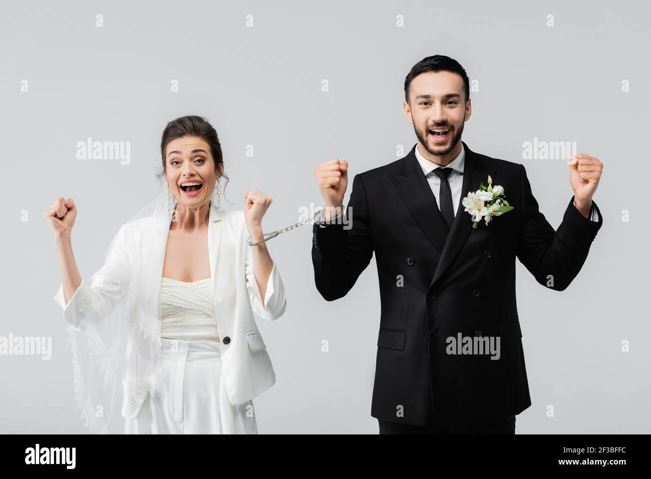 Mariée interraciale excitée et marié dans les menottes montrant ouais isolé en gris Banque D'Images