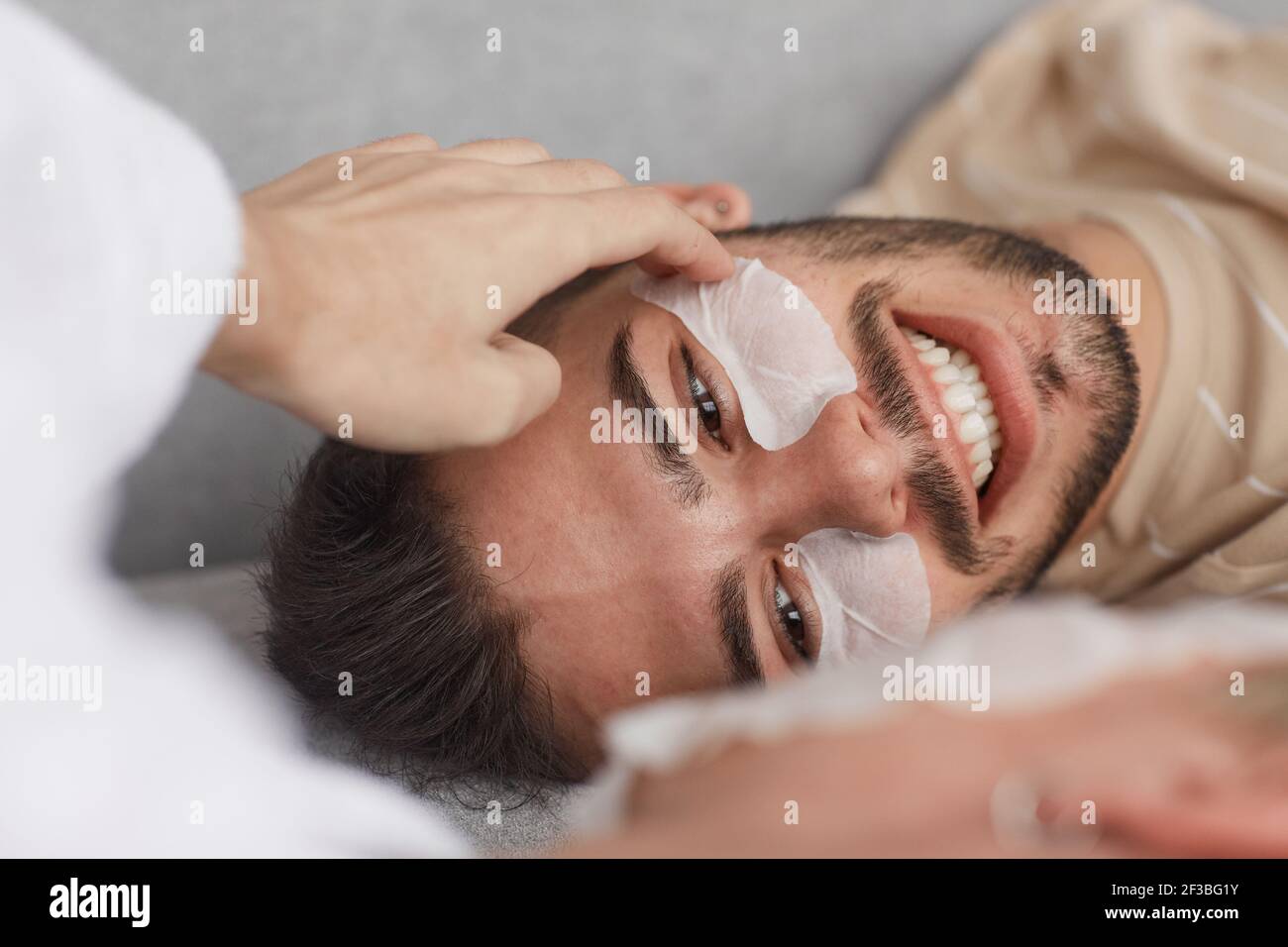 Gros plan d'un jeune homme souriant portant des patches de visage tout en étant allongé sur un canapé avec un petit ami, espace de copie Banque D'Images