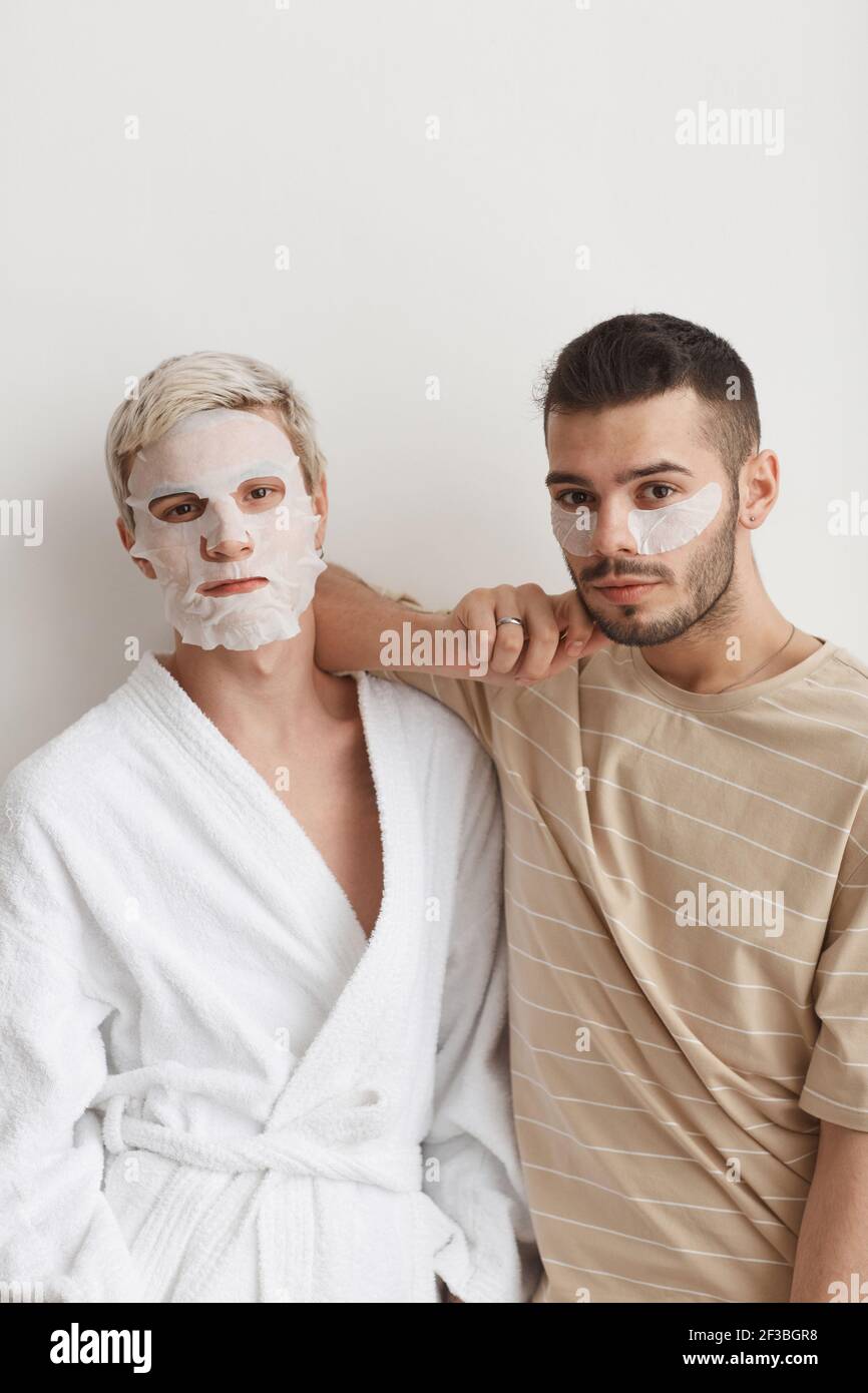 Petit portrait de jeune couple gay regardant appareil photo tout en portant des masques pour le visage pendant la routine de beauté à la maison Banque D'Images