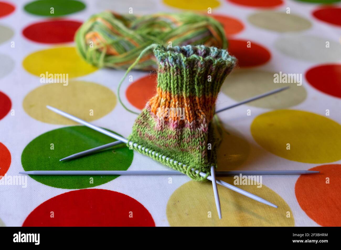 Chaussette verte et orange tricotée sur 4 aiguilles à tricoter sur une nappe en toile d'huile, tachegloth orange vert jaune cercles R.-U. KATHY DEWITT Banque D'Images