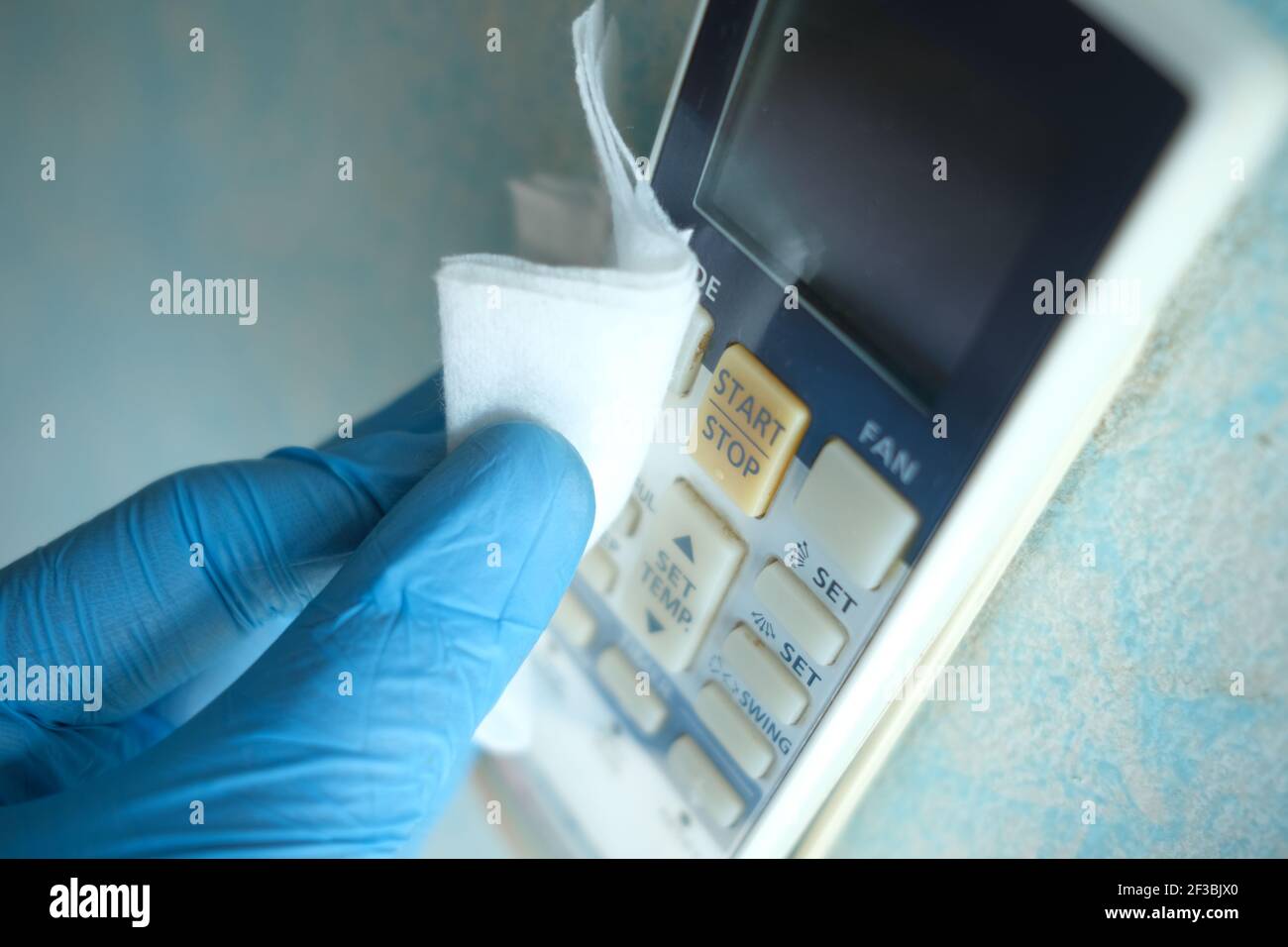 mains dans des gants en caoutchouc bleu pour nettoyer la télécommande de climatisation Banque D'Images