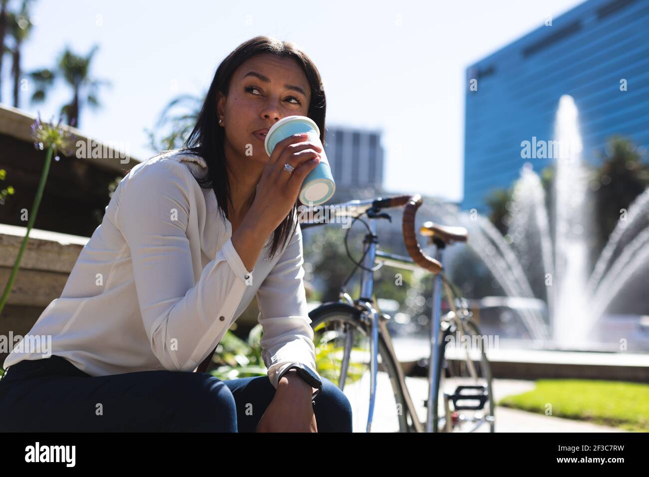 Femme de race mixte assise dans le parc buvant du café Banque D'Images