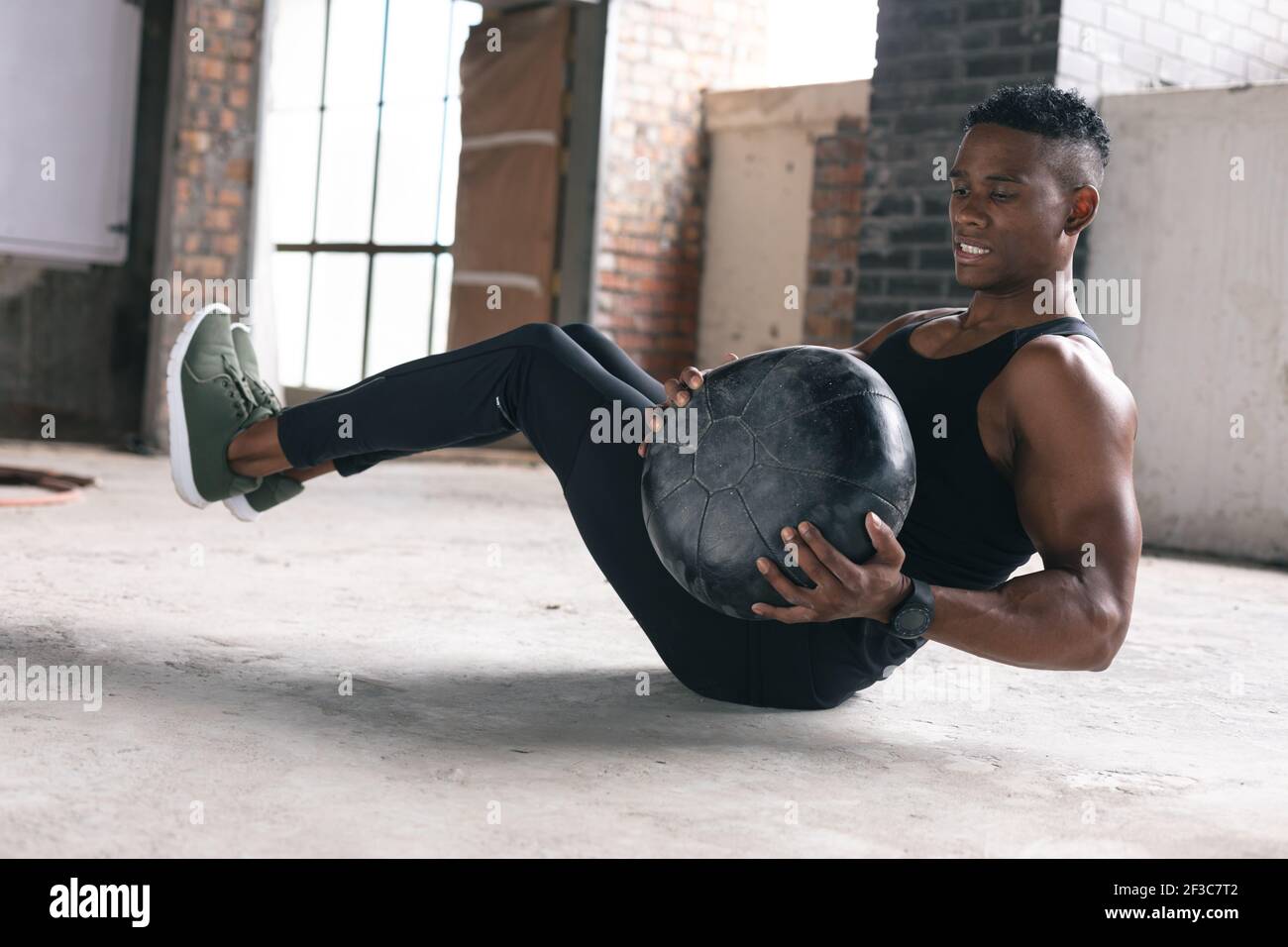 Afro-américain homme s'exerçant dans un entrepôt faisant des sit-ups tenue ballon de médecine Banque D'Images