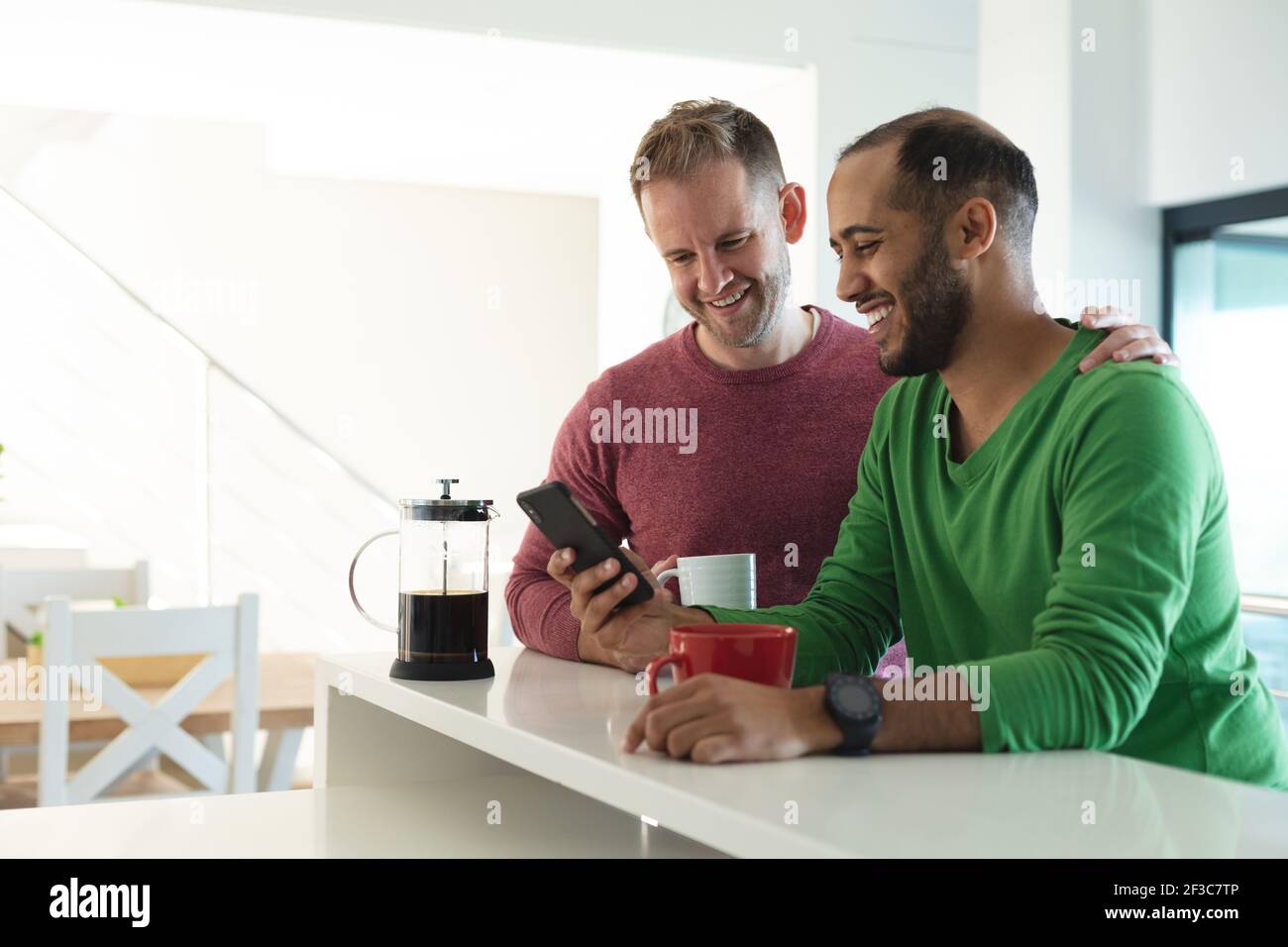 Couple multi-ethnique gay masculin souriant et utilisant le smartphone dans cuisine à la maison Banque D'Images