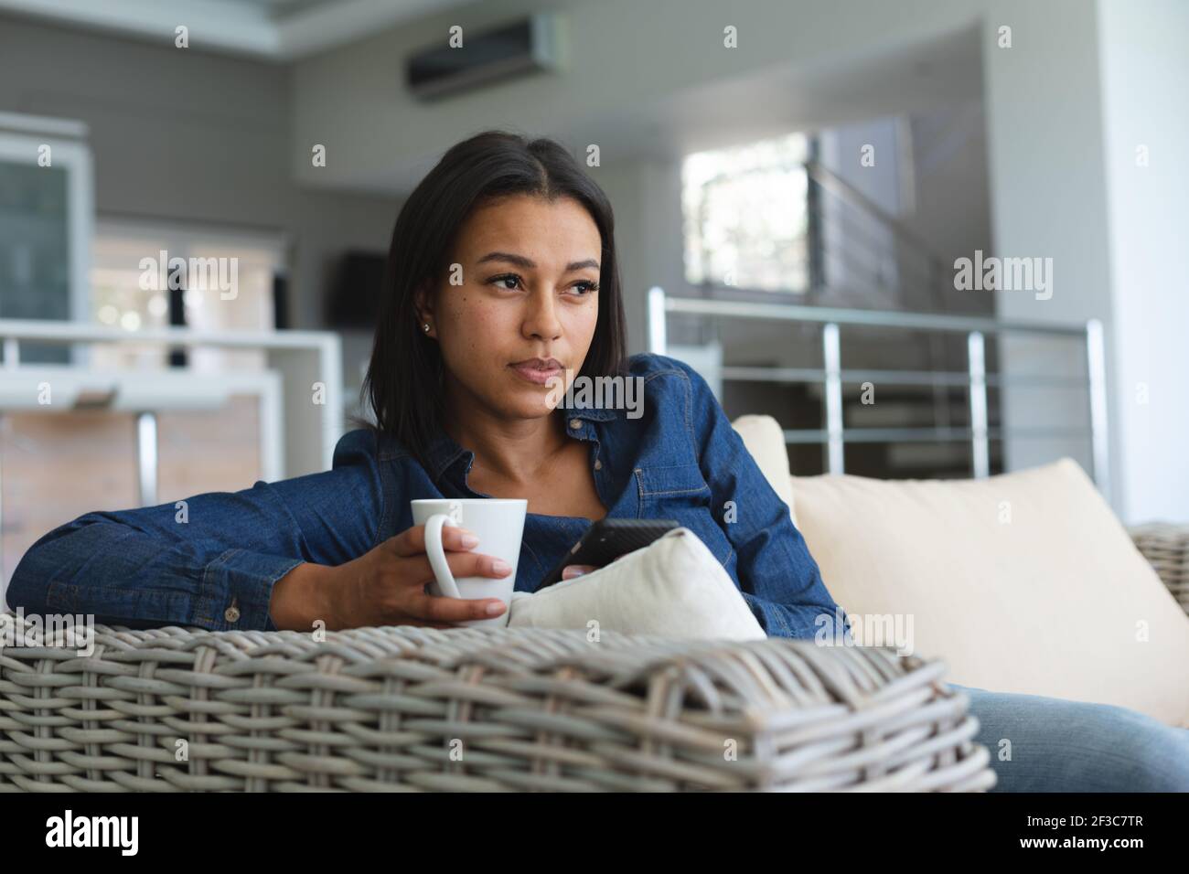 Femme de race mixte se détendant dans le salon sur le canapé avec une tasse de café Banque D'Images