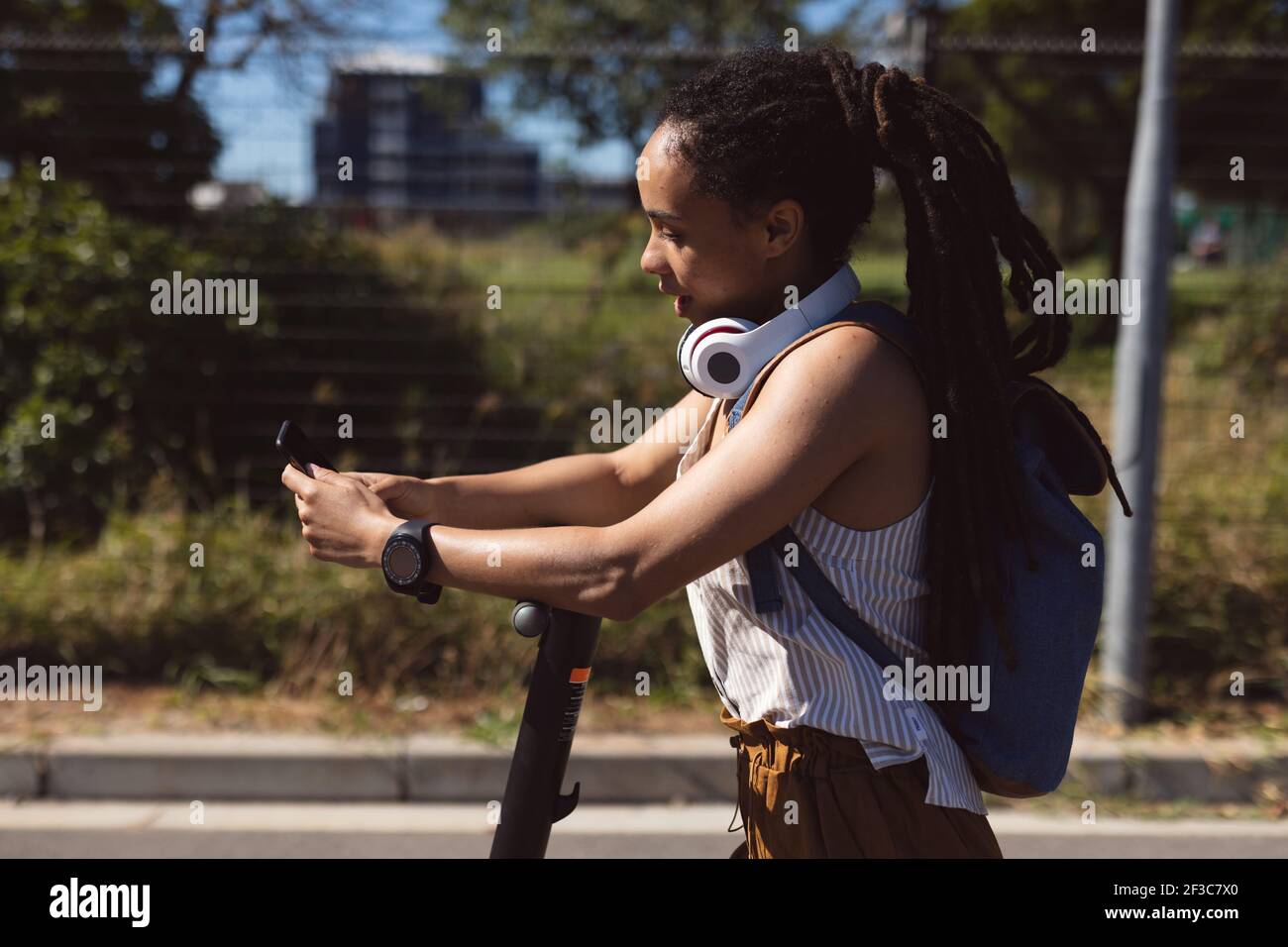 Femme afro-américaine portant un casque avec un scooter et utilisant un smartphone rue Banque D'Images