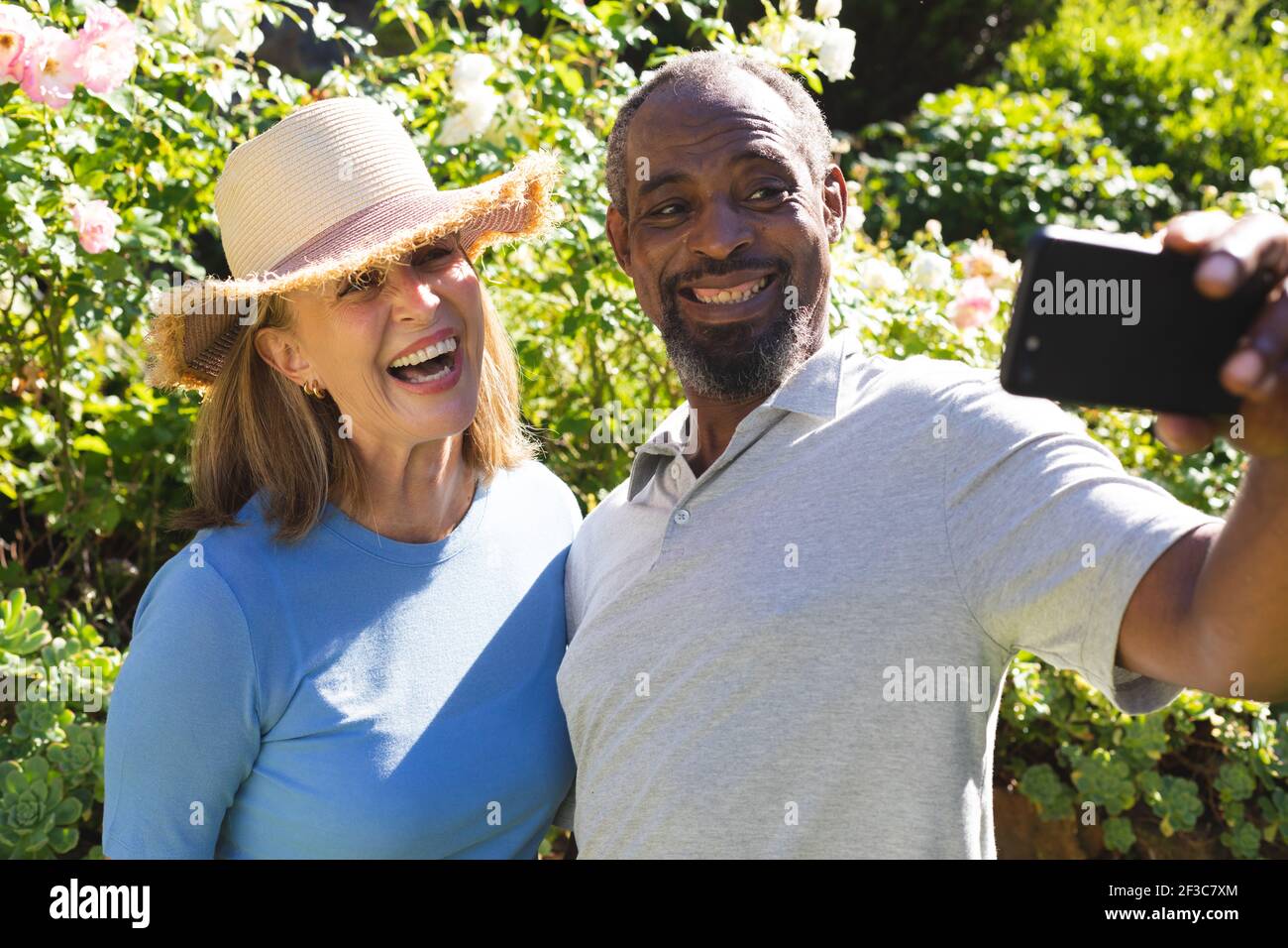 Couple senior varié dans le jardin prenant le selfie avec un smartphone Banque D'Images