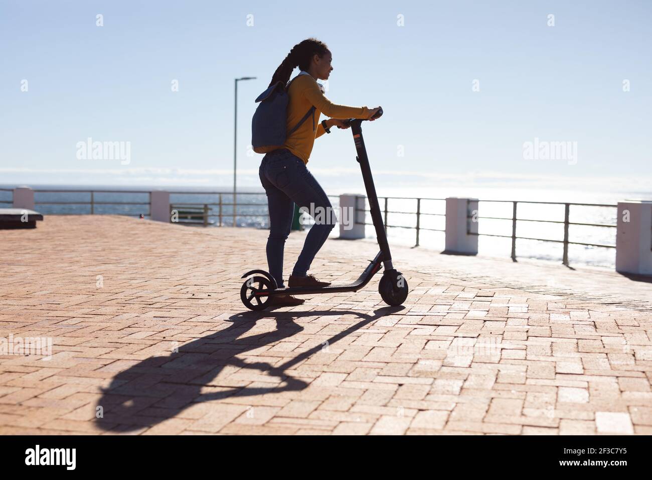 Femme afro-américaine souriante admirant la vue sur la mer avec un scooter promenade au bord de la mer Banque D'Images