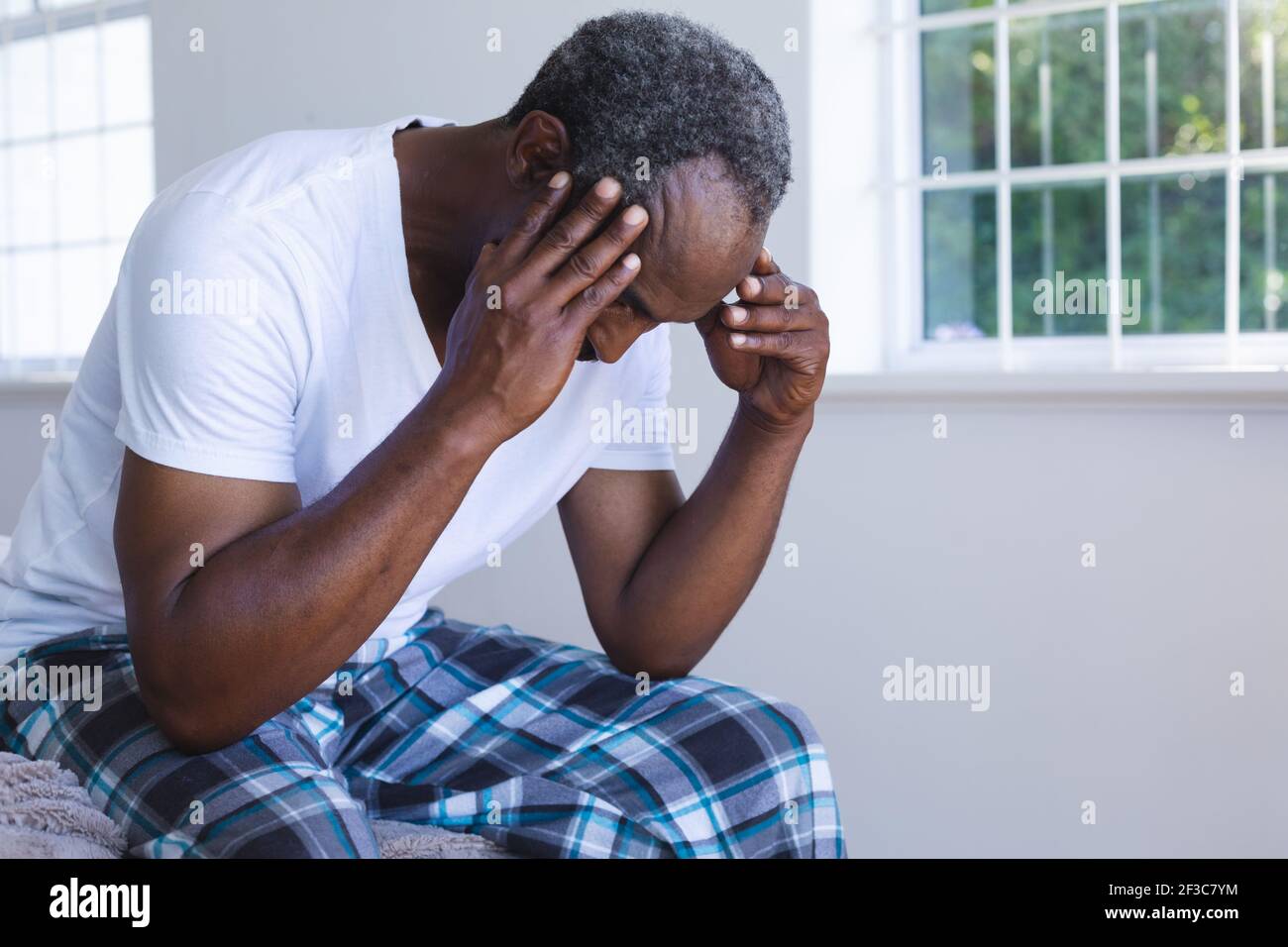 Homme senior de race mixte assis sur le lit et tenant son tête Banque D'Images