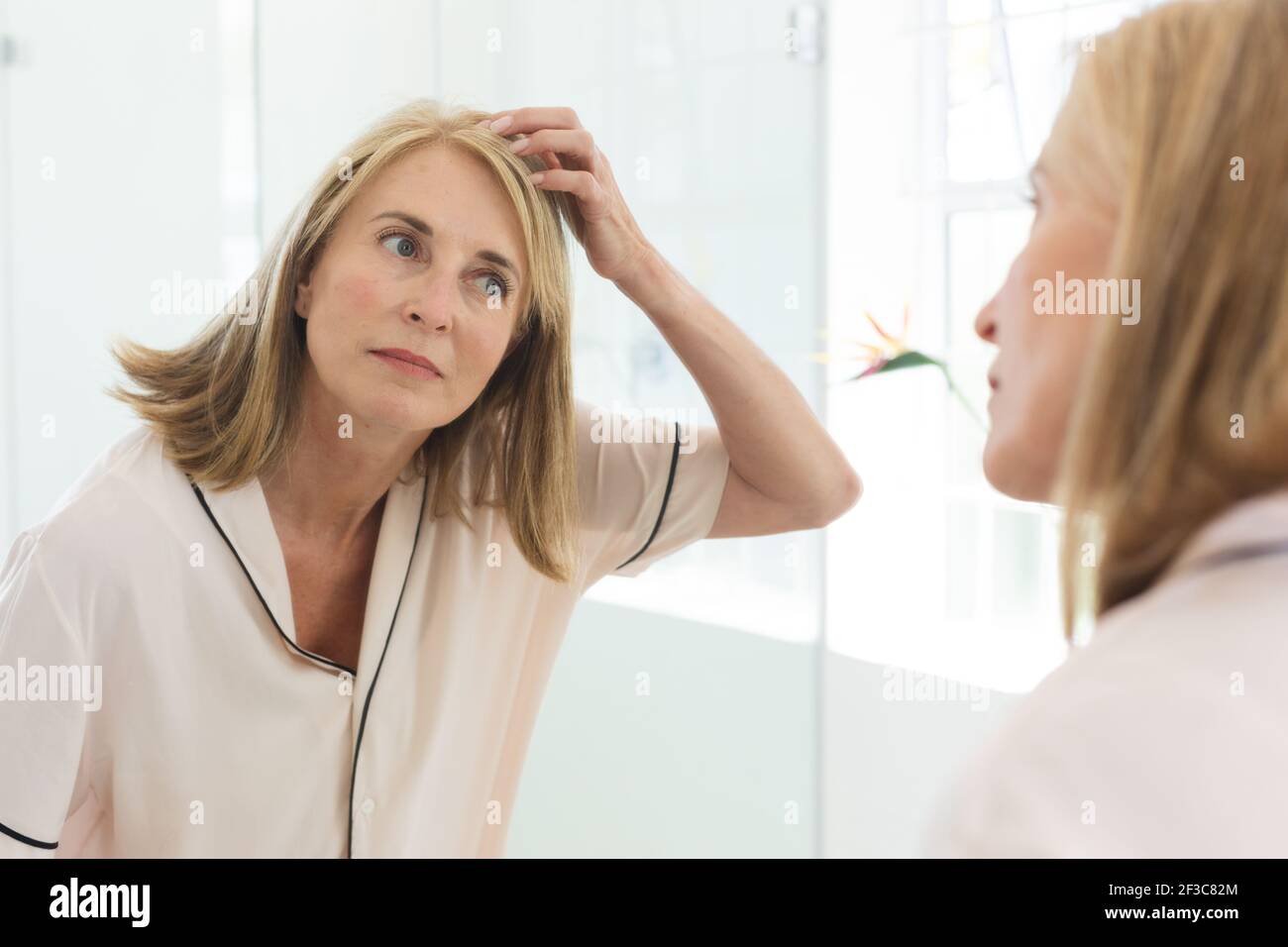 Femme de race blanche debout dans la salle de bains faisant ses cheveux Banque D'Images