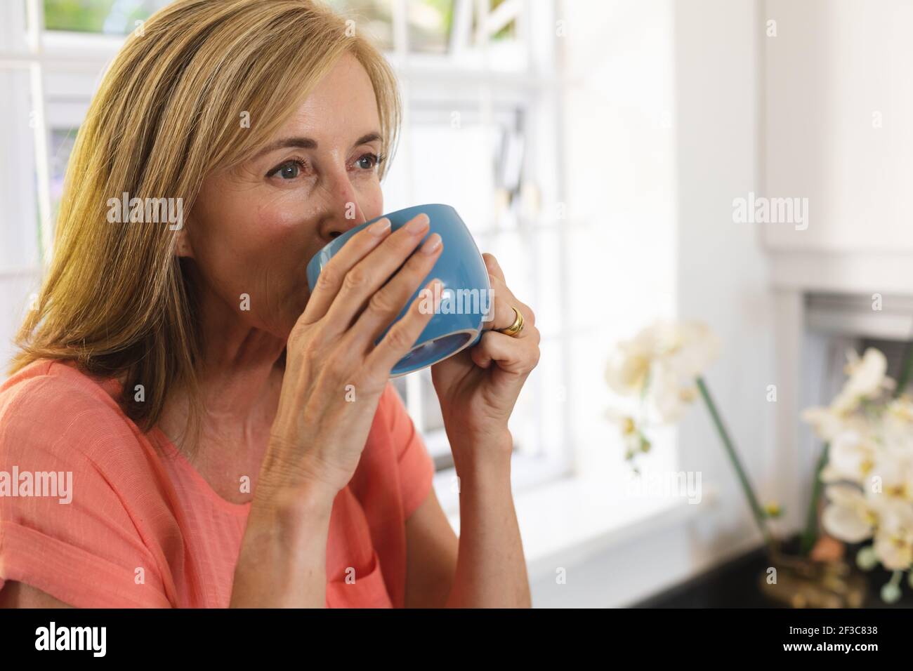 Femme de race blanche debout près de la fenêtre buvant une tasse de café Banque D'Images