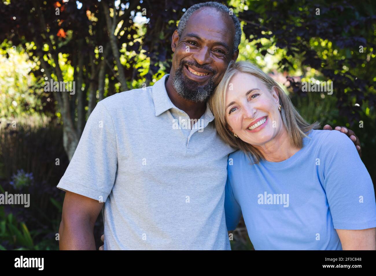 Portrait d'un couple senior varié dans le jardin regardant l'appareil photo et souriant Banque D'Images