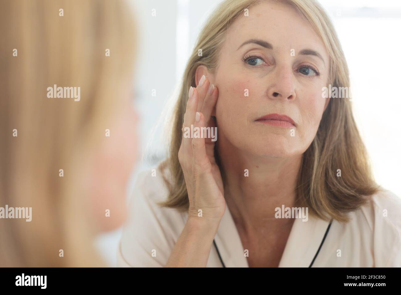 Femme de race blanche debout dans la salle de bains mettant de la crème sur le visage Banque D'Images