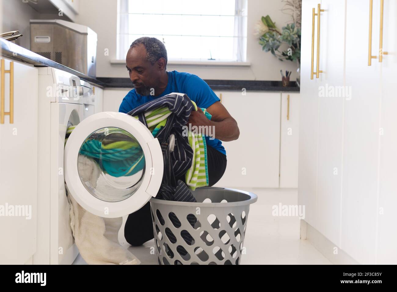 Homme senior de course mixte chargé d'une machine à laver Banque D'Images