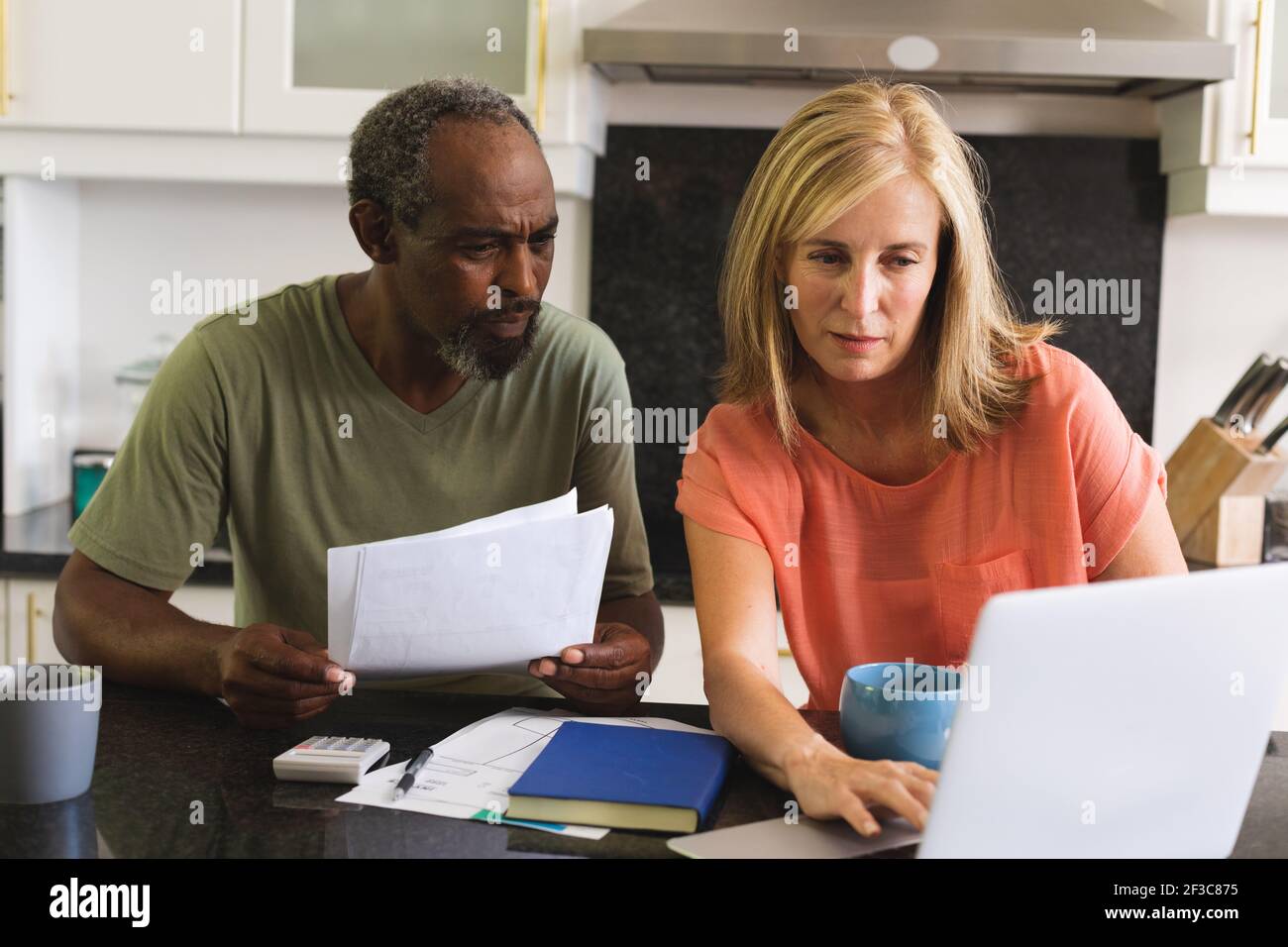 Divers couples âgés assis dans la cuisine avec un ordinateur portable et en allant par la paperasserie Banque D'Images