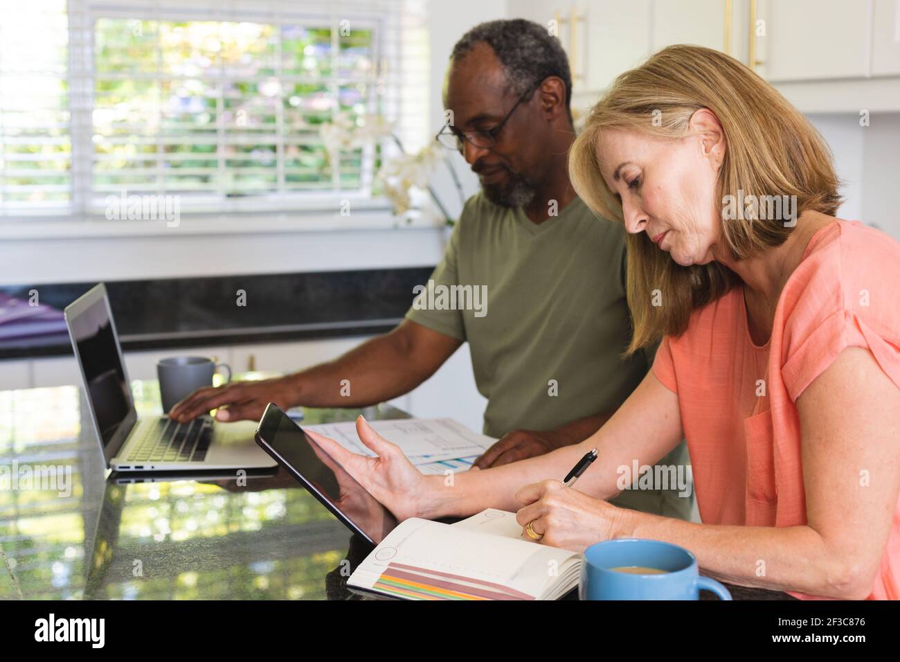 Divers couples âgés assis dans la cuisine avec un ordinateur portable et en allant par la paperasserie Banque D'Images