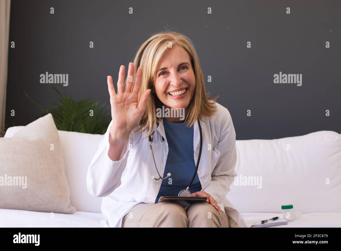 Femme de race blanche médecin assis sur un canapé souriant donnant la vidéo appelez la consultation Banque D'Images