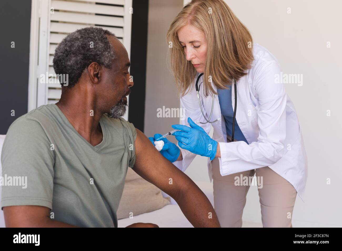 Femme de race blanche médecin senior vaccinant l'homme âgé de race mixte Banque D'Images