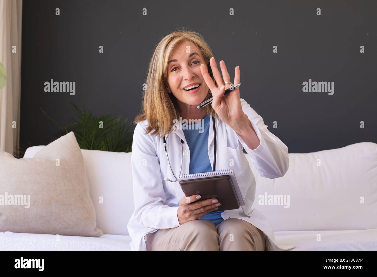 Femme de race blanche médecin assis sur un canapé souriant donnant la vidéo appelez la consultation Banque D'Images