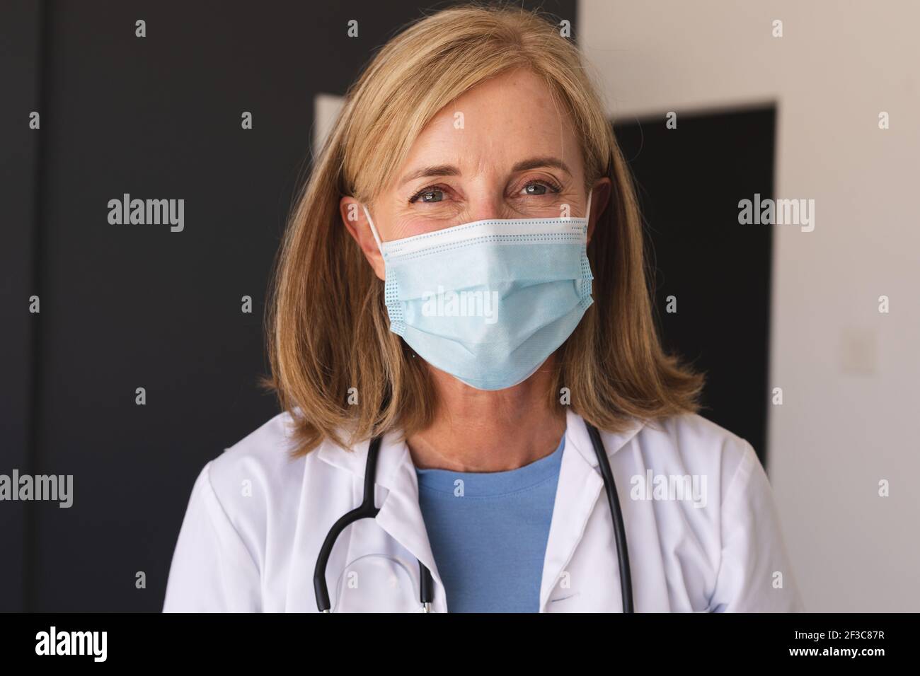 Femme de race blanche, médecin sénior portant un masque facial regardant appareil photo et sourire Banque D'Images