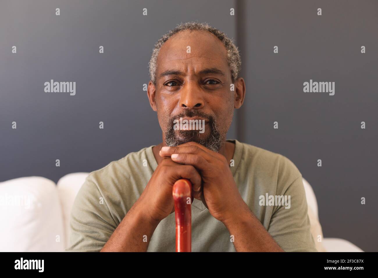 Portrait d'un homme senior de race mixte assis sur un canapé tenant canne regardant l'appareil photo et souriant Banque D'Images