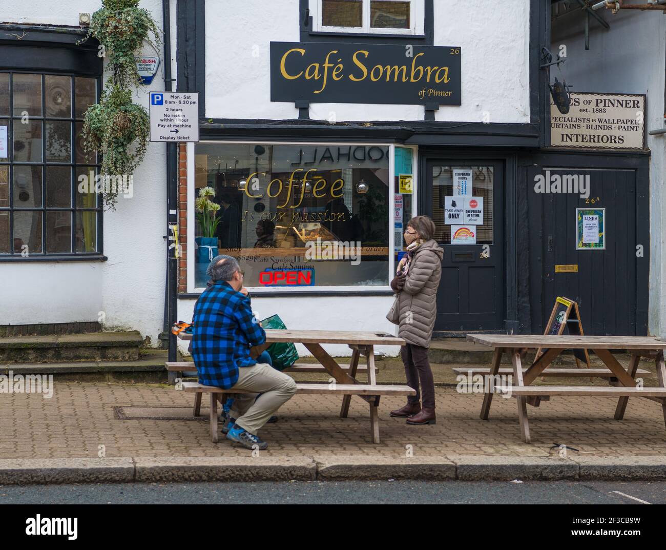 Un couple assis à une table de trottoir en conversation avec une femme debout portant un masque facial à l'extérieur du café Sombra, High Street, Pinner. Banque D'Images