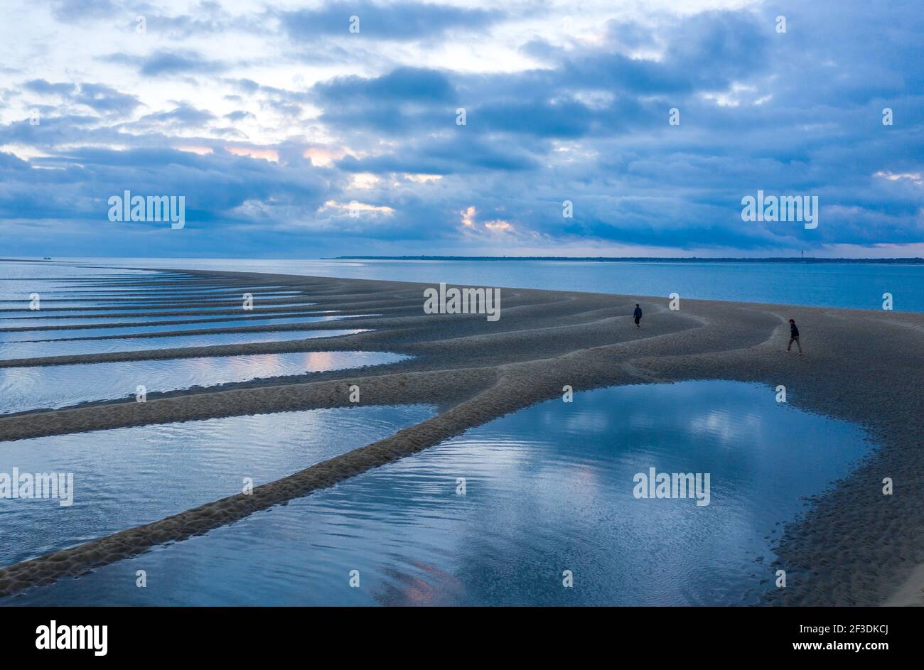 Personnes explorant des affleurements de sable dans la mer à marée basse. Vue en grand angle du paysage côtier au crépuscule. Banque D'Images