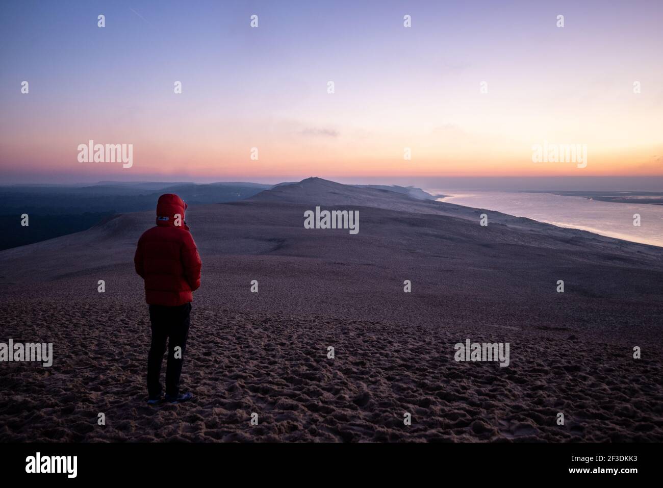 Personne en vêtements chauds avec sweat à capuche sur la tête debout sur la plage de sable et appréciant le coucher de soleil d'hiver coloré. Banque D'Images