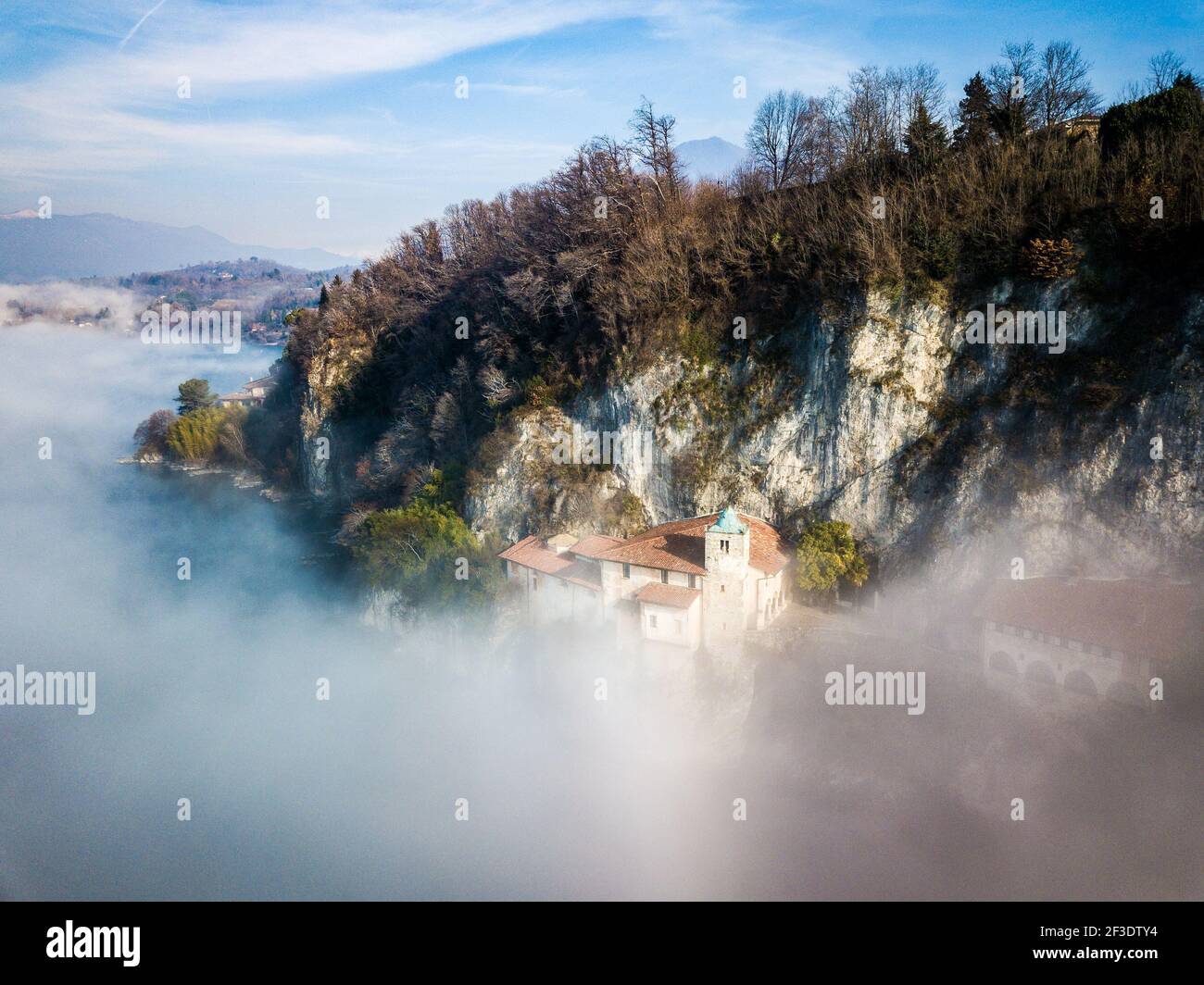 Vue aérienne sur les bâtiments sous le mur de roche de l'affleurement jusqu'au lac. Journée ensoleillée au-dessus du brouillard qui s'élève de la surface de l'eau. Banque D'Images