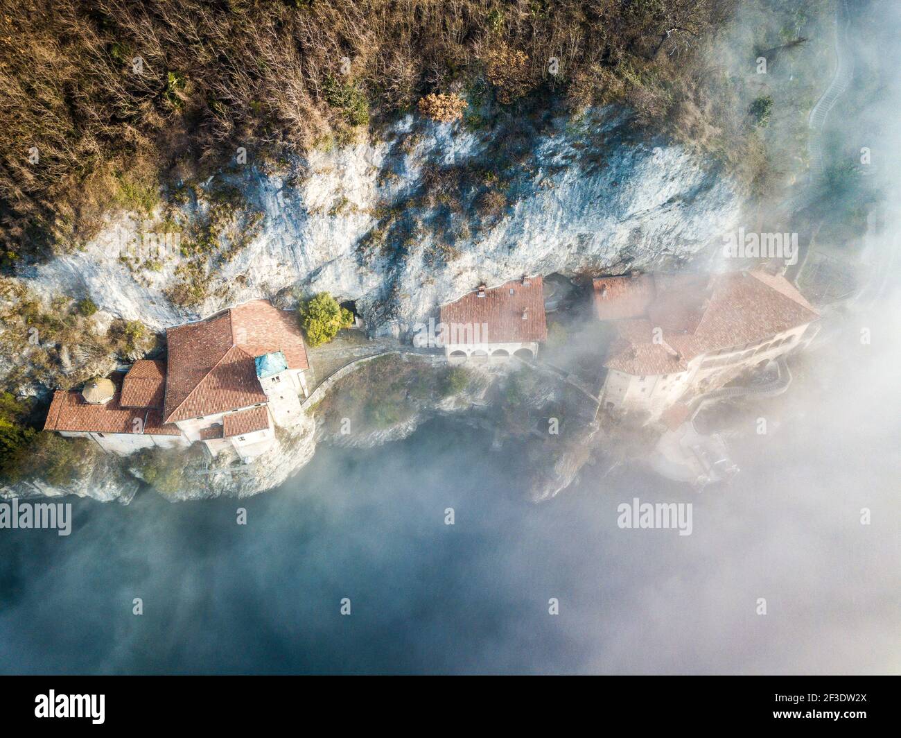 Vue de dessus en bas sur plusieurs maisons bloquées sur la roche au-dessus de la surface de l'eau. Le soleil brille sur les toits au-dessus du brouillard clairsemé. Banque D'Images