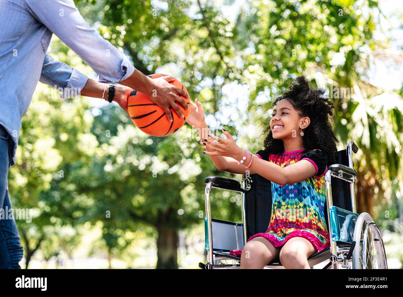 Petite fille en fauteuil roulant jouant au basket-ball avec son père. Banque D'Images