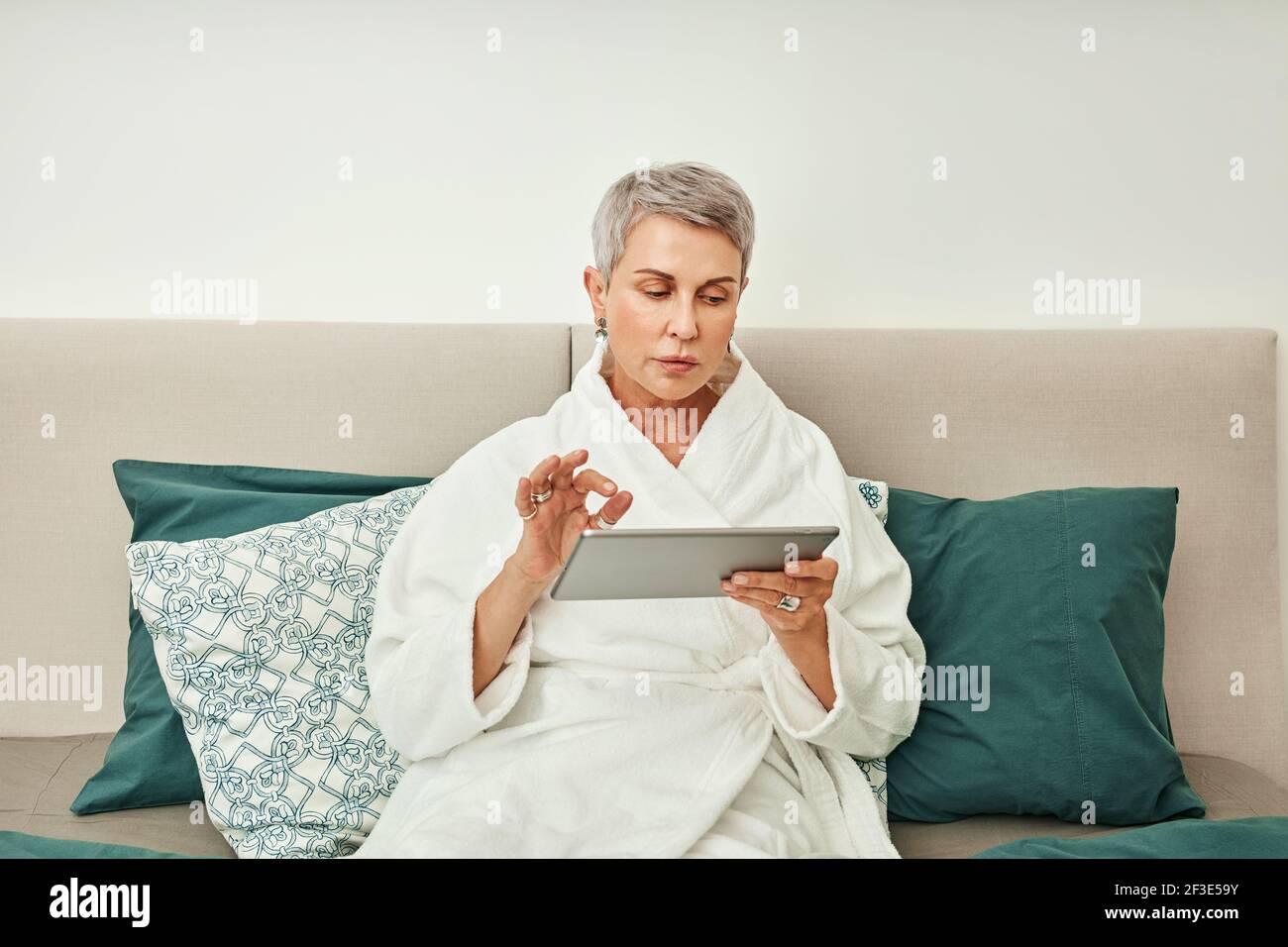 Femme mûre avec cheveux gris à l'aide d'une tablette numérique dans chambre Banque D'Images