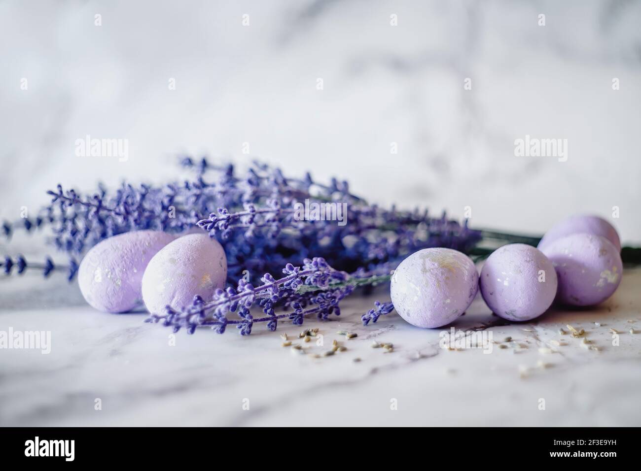 Oeufs de Pâques violets sur une table avec fleurs de lavande bleues. Banque D'Images