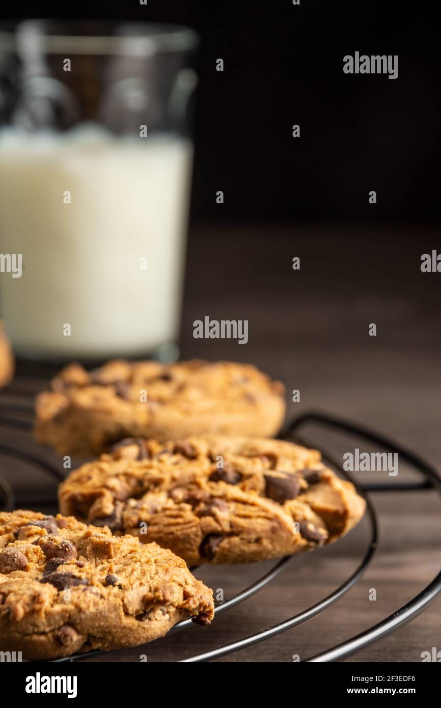 Gros plan de cookies au chocolat sur un support métallique, un verre de lait, une mise au point sélective, sur une table en bois, verticale, avec espace de copie Banque D'Images