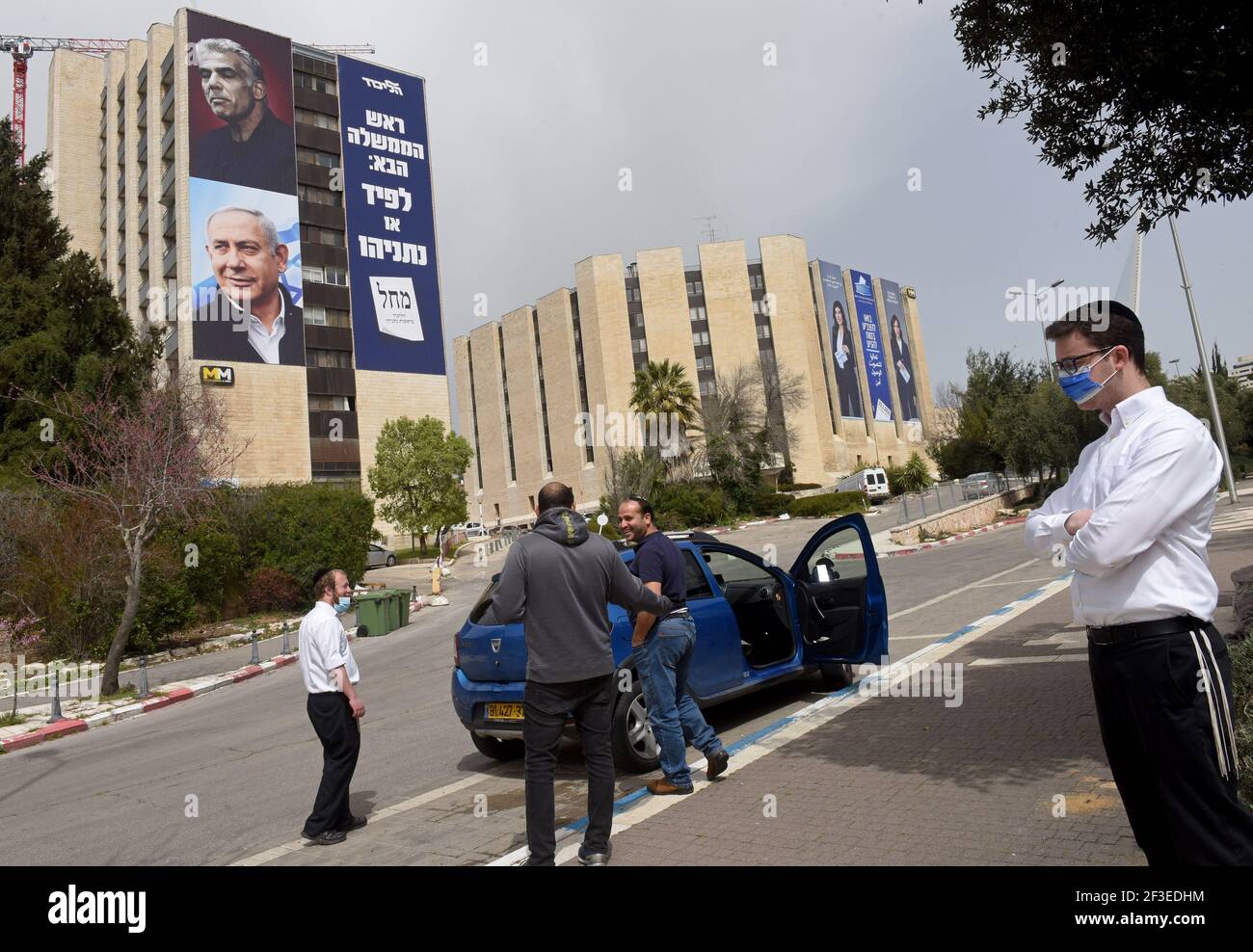 Jérusalem, Israël. 15 mars 2021. Les Israéliens se tiennent dans la rue près d'une bannière électorale pour le Likoud avec son chef, le Premier ministre Benjamin Netanyahu (bas) et le chef de l'opposition Yair Lapid (haut), dans un immeuble à Jérusalem, le lundi 15 mars 2021. Netanyahou fait face à sa quatrième tentative de réélection depuis deux ans, lorsque les Israéliens vont aux urnes le 23 mars. Photo par Debbie Hill/UPI crédit: UPI/Alay Live News Banque D'Images