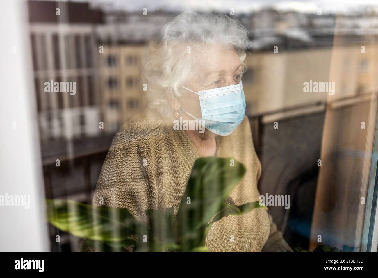 Femme âgée avec masque de visage regardant par la fenêtre à accueil Banque D'Images