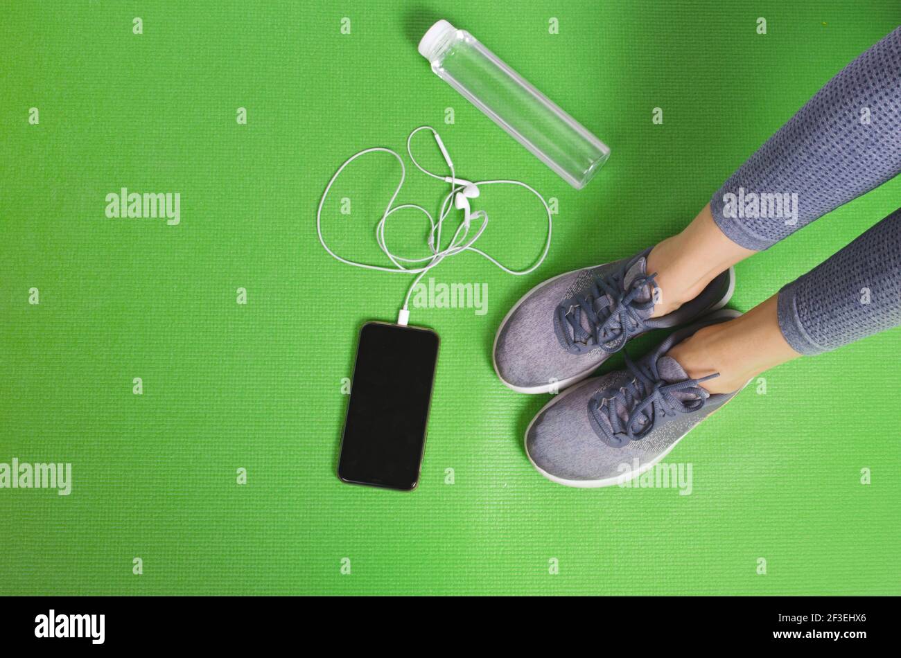 Femme sport jambes sur tapis vert yoga avec téléphone et bouteille de boisson Banque D'Images