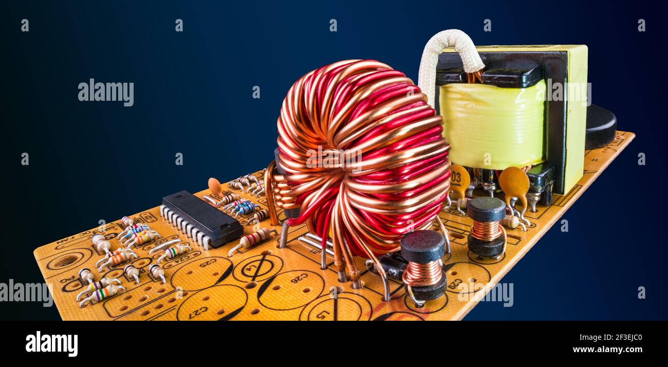 Composants électroniques dans la carte de circuit imprimé orange volant sur fond bleu foncé. Scène abstraite. Bobines de noyau en ferrite, résistances, puce, transformateur sur ci. Banque D'Images