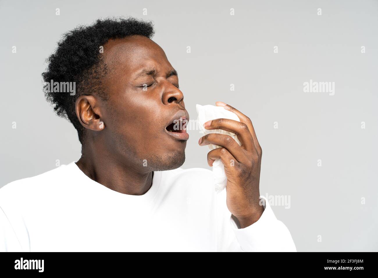 L'homme noir soufflant le nez et éternuant dans les tissus ou la serviette, a l'allergie, les premiers symptômes du rhume et de la grippe Banque D'Images