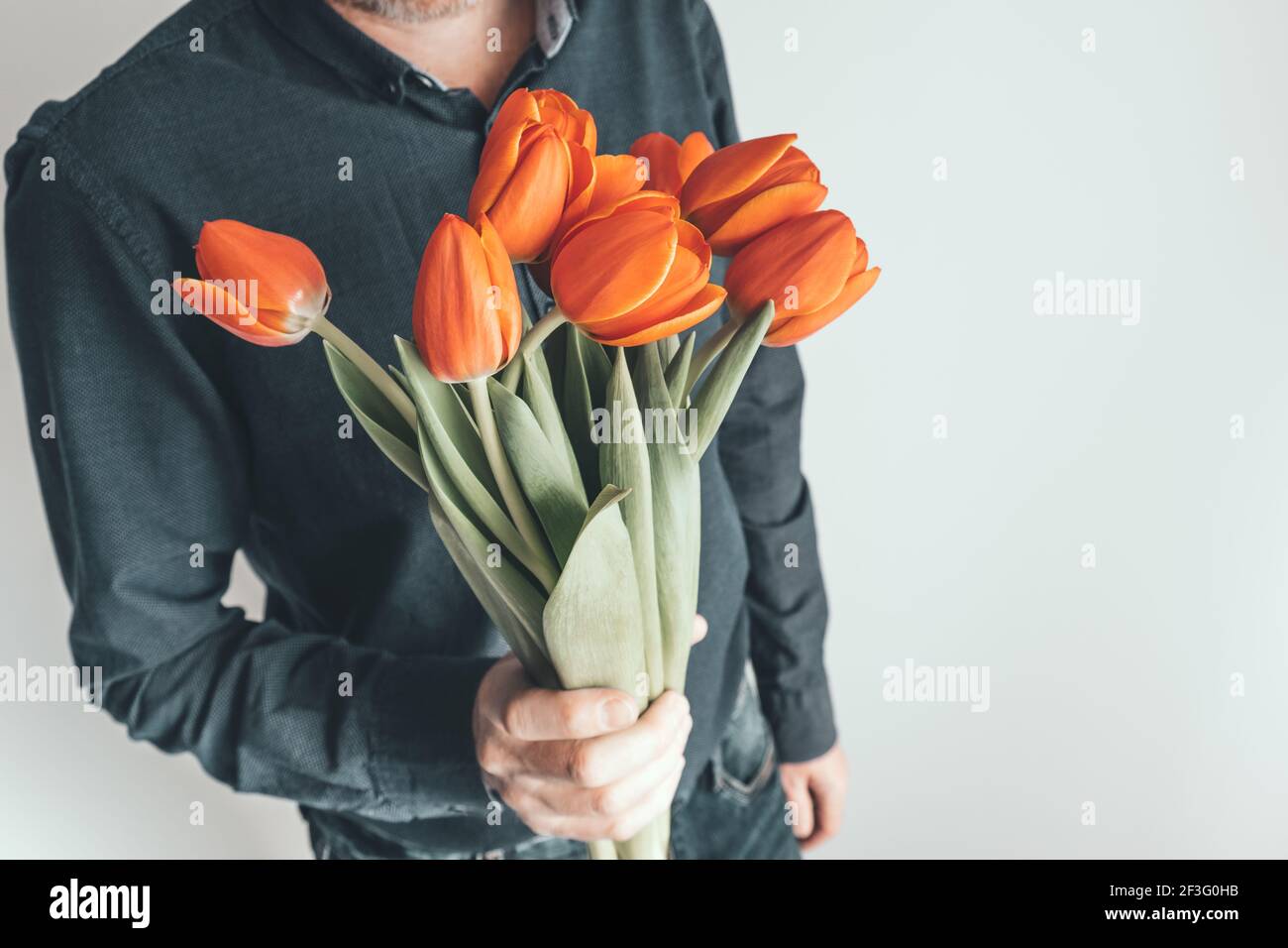 Un homme tient un bouquet de fleurs devant lui. Tulipes orange vif comme cadeau pour l'anniversaire, la Saint-Valentin, la Fête des mères, la Journée internationale de la femme. Banque D'Images