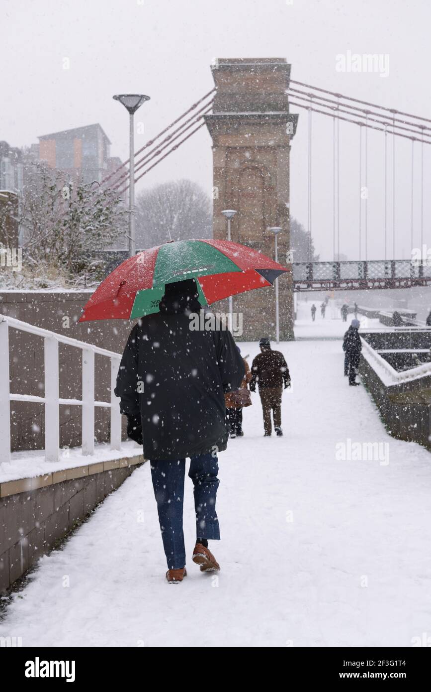 Un homme avec un parapluie de golf marchant sur la passerelle de Clyde couverte de neige en direction du pont suspendu de Portland Street à Glasgow, en Écosse, au Royaume-Uni Banque D'Images