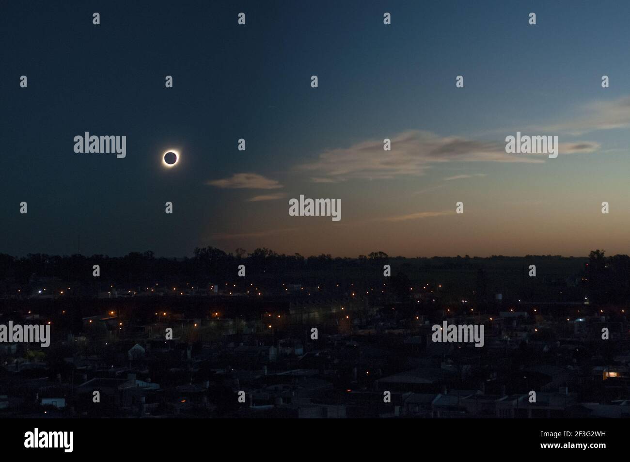 Une éclipse solaire totale pendant la soirée au-dessus d'un moderne ville entourée de bâtiments, arbres et lumières Banque D'Images