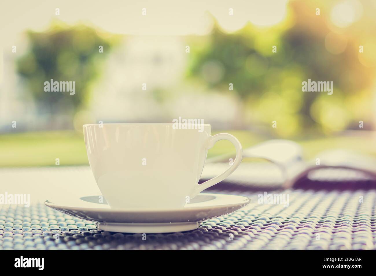 Tasse à café avec livre sur la table en vert flou arrière-plan nature - couleurs de style vintage Banque D'Images