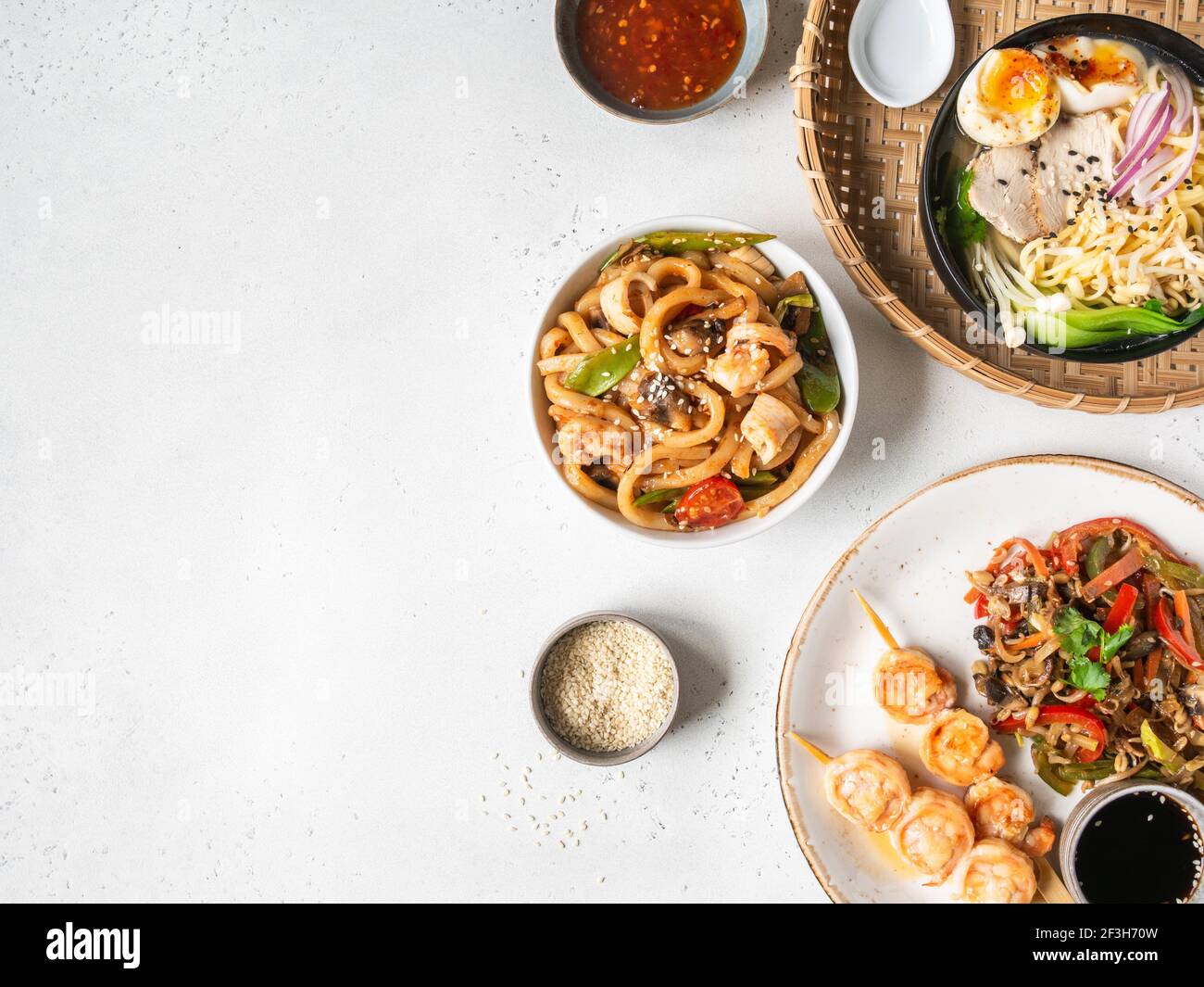 Set de cuisine asiatique - soupe de ramen, crevettes grillées, légumes sautés et udon avec fruits de mer sur fond blanc. Vue de dessus. Copier l'espace. Pose à plat Banque D'Images