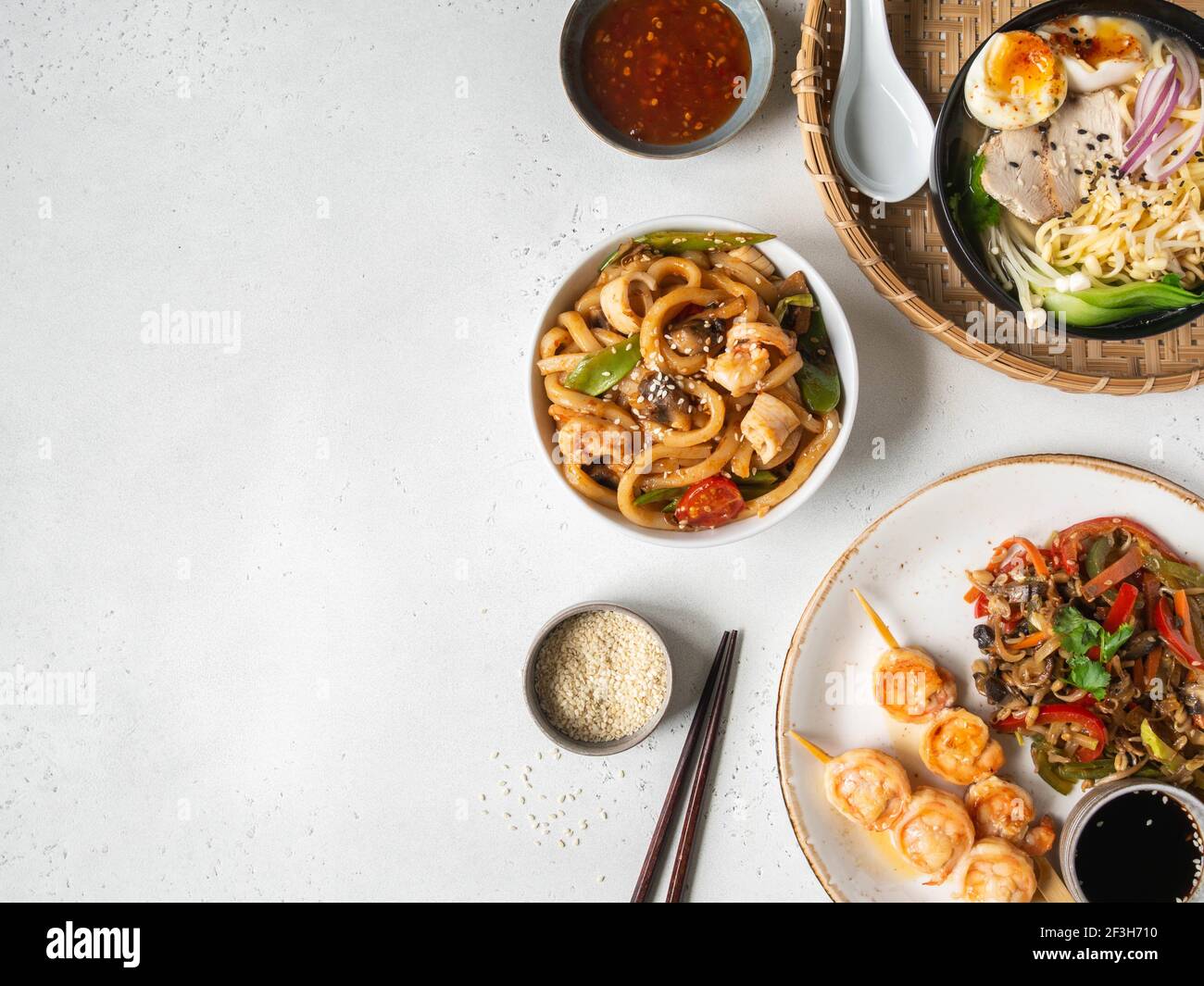 Set de cuisine asiatique - soupe de ramen, crevettes grillées, légumes sautés et udon avec fruits de mer sur fond blanc. Vue de dessus. Copier l'espace. Pose à plat Banque D'Images